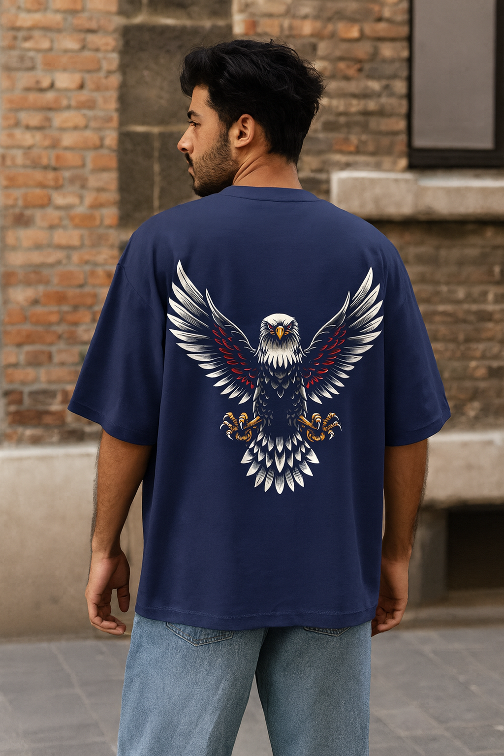 Man wearing a navy blue t-shirt with an eagle design on the back, standing against a brick wall.
