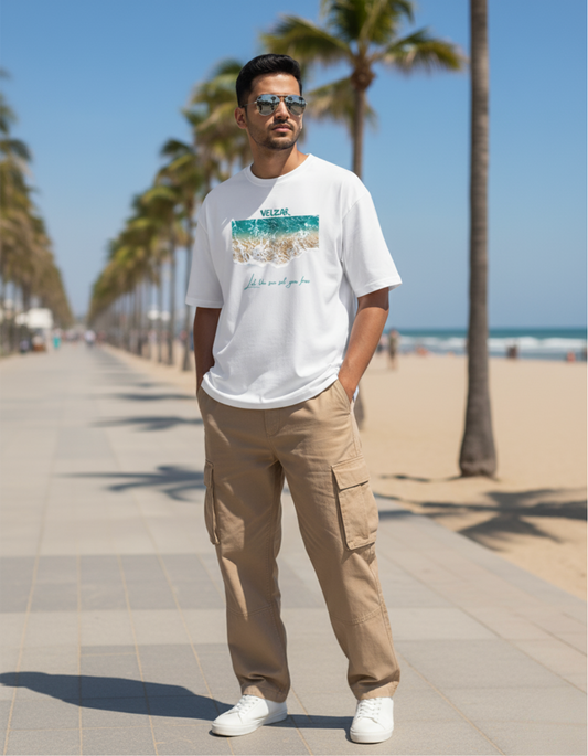 Man standing on a beach promenade with palm trees and ocean drift t-shirt and an ocean in the background