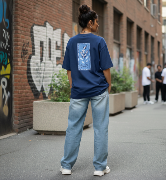 Person wearing a blue t-shirt with a floral design and light blue jeans standing on a street with graffiti.