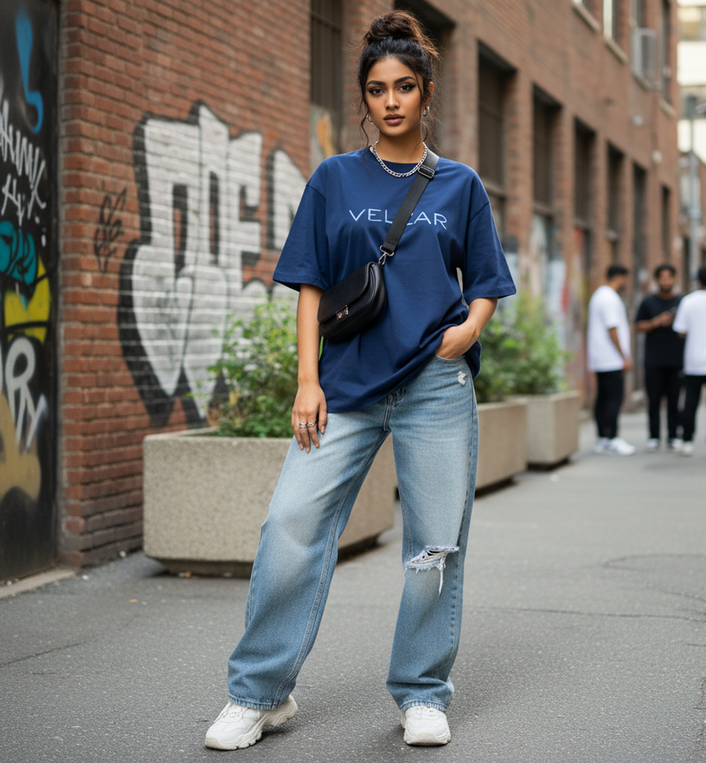 Woman wearing a blue t-shirt and jeans standing on a street with graffiti in the background